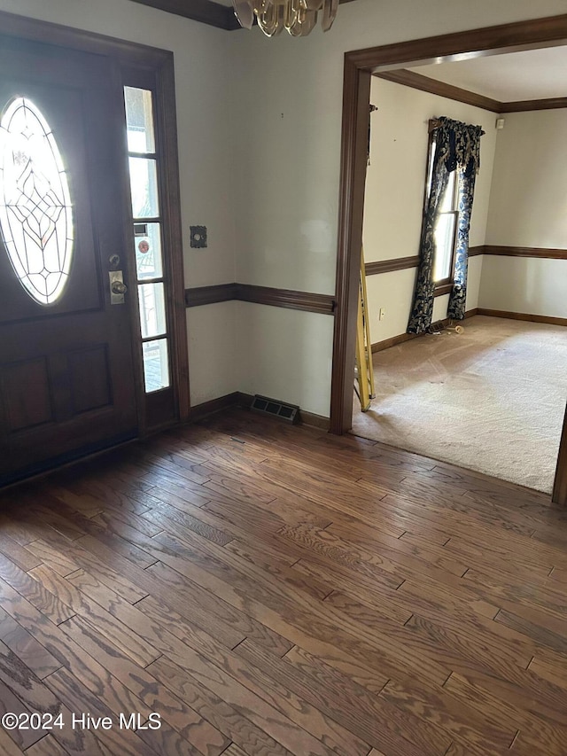 entryway with a notable chandelier, crown molding, and dark wood-type flooring