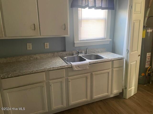 kitchen with white cabinetry, sink, water heater, light stone counters, and wood-type flooring