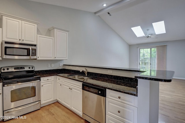 kitchen featuring sink, stainless steel appliances, kitchen peninsula, lofted ceiling with skylight, and white cabinets