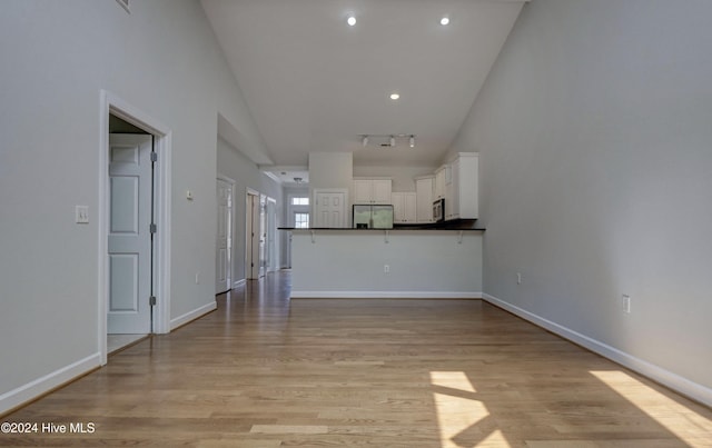 unfurnished living room featuring light hardwood / wood-style flooring, rail lighting, and vaulted ceiling