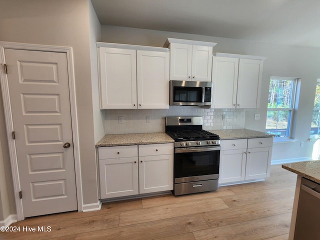 kitchen with white cabinets, decorative backsplash, light stone countertops, and appliances with stainless steel finishes