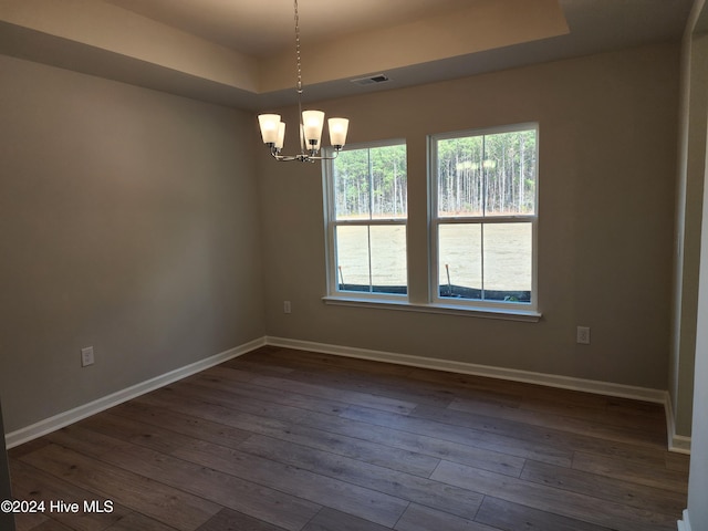 empty room with a raised ceiling, dark wood-type flooring, and an inviting chandelier