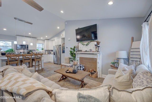 living room featuring ceiling fan, a healthy amount of sunlight, light hardwood / wood-style floors, and vaulted ceiling