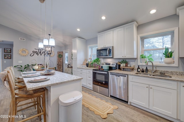 kitchen featuring stainless steel appliances, sink, pendant lighting, white cabinets, and a center island