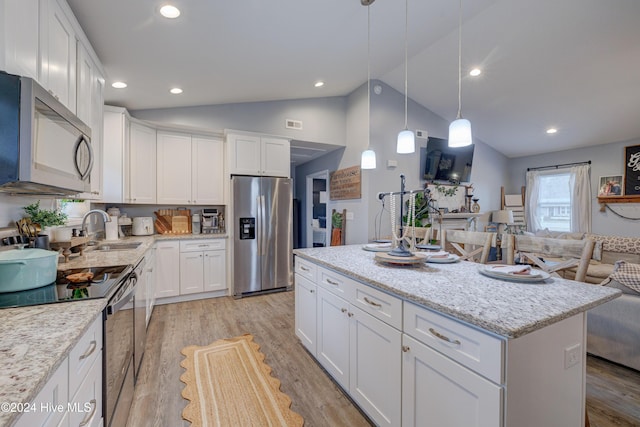 kitchen with lofted ceiling, white cabinets, sink, appliances with stainless steel finishes, and a kitchen island