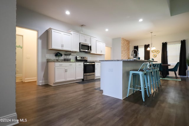 kitchen with hanging light fixtures, dark hardwood / wood-style floors, a center island with sink, white cabinets, and appliances with stainless steel finishes