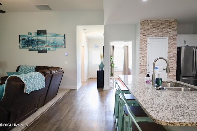 kitchen with green cabinets, sink, stainless steel fridge, an island with sink, and dark hardwood / wood-style flooring