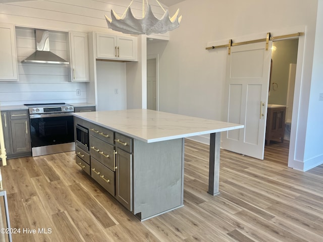 kitchen with appliances with stainless steel finishes, gray cabinetry, wall chimney range hood, a barn door, and light hardwood / wood-style floors