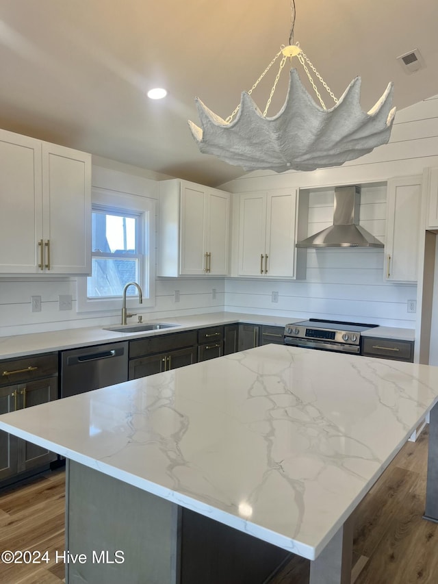 kitchen with light stone countertops, a kitchen island, hanging light fixtures, and wall chimney exhaust hood