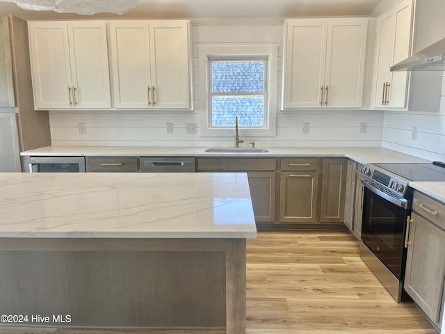 kitchen featuring wall chimney range hood, sink, light hardwood / wood-style flooring, appliances with stainless steel finishes, and light stone counters