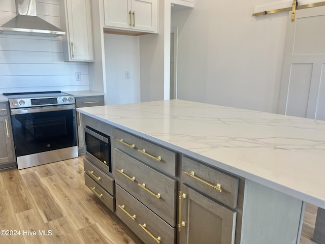 kitchen featuring wall chimney range hood, a barn door, gray cabinets, appliances with stainless steel finishes, and light wood-type flooring