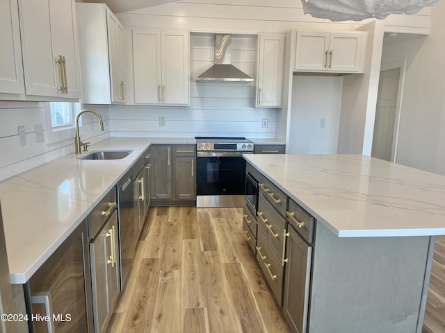 kitchen with stainless steel range with electric stovetop, a center island, wall chimney range hood, sink, and light wood-type flooring