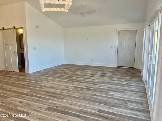 unfurnished room featuring a barn door, high vaulted ceiling, light hardwood / wood-style flooring, and ceiling fan