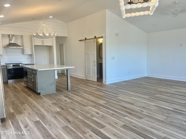 kitchen with white cabinetry, a center island, wall chimney range hood, a barn door, and stainless steel stove