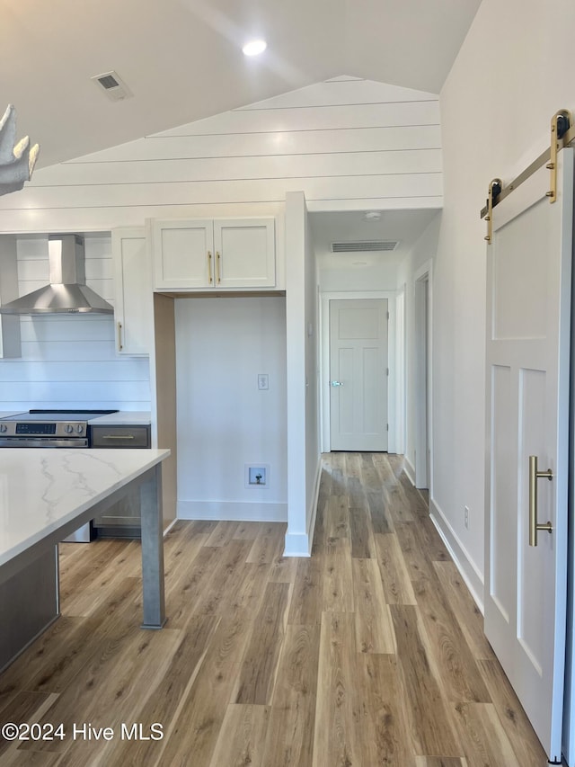 kitchen featuring light stone countertops, wall chimney exhaust hood, vaulted ceiling, a barn door, and white cabinets