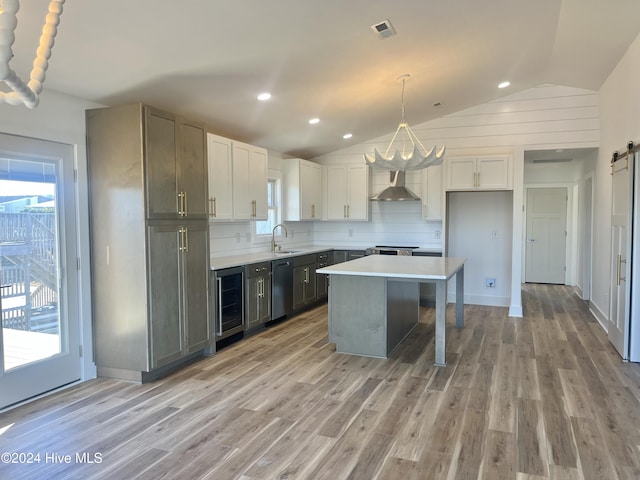 kitchen featuring a center island, wall chimney range hood, light hardwood / wood-style flooring, pendant lighting, and appliances with stainless steel finishes