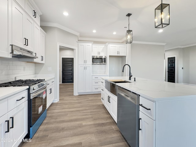 kitchen featuring appliances with stainless steel finishes, light wood-type flooring, a kitchen island with sink, pendant lighting, and white cabinets