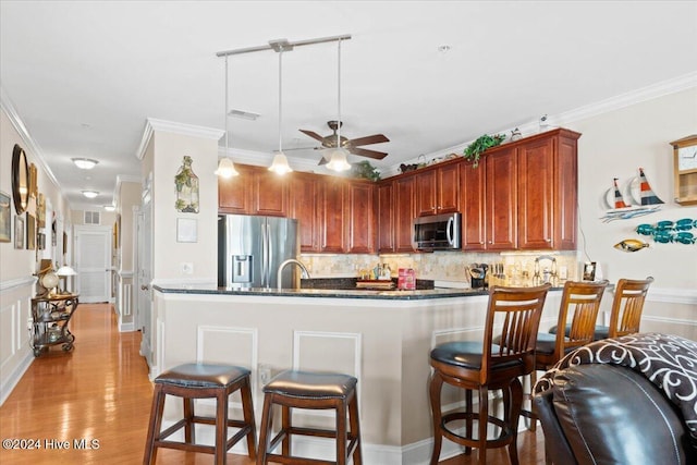 kitchen featuring backsplash, crown molding, hanging light fixtures, appliances with stainless steel finishes, and kitchen peninsula