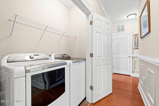 laundry room with light hardwood / wood-style floors, ornamental molding, and washing machine and clothes dryer