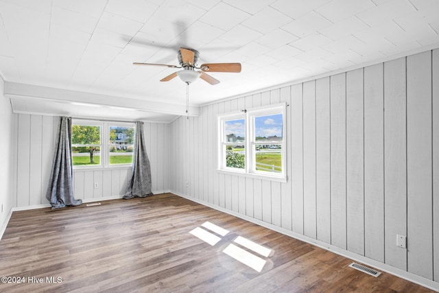 unfurnished room with a wealth of natural light, hardwood / wood-style floors, ceiling fan, and wood walls