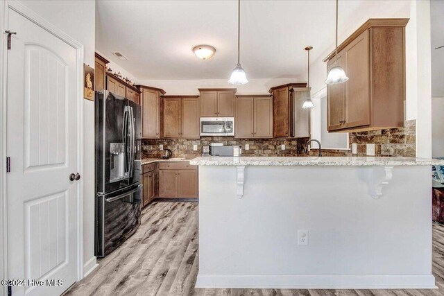 kitchen featuring light stone countertops, a breakfast bar, black fridge with ice dispenser, light hardwood / wood-style floors, and hanging light fixtures