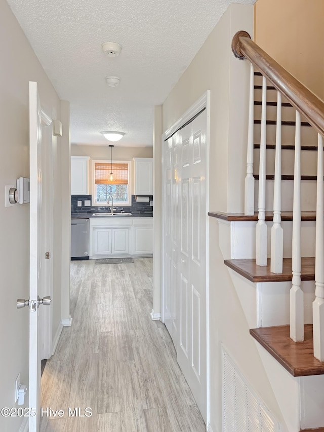 hallway with sink, light hardwood / wood-style flooring, and a textured ceiling