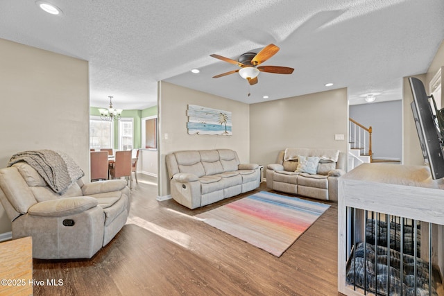 living room with wood-type flooring, ceiling fan with notable chandelier, and a textured ceiling