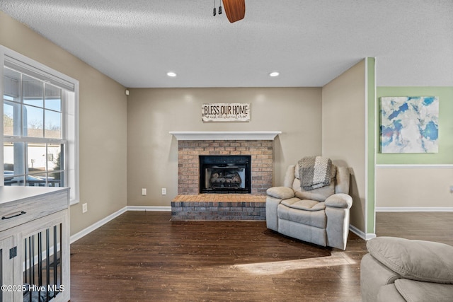 living room featuring dark hardwood / wood-style flooring, a brick fireplace, a textured ceiling, and ceiling fan