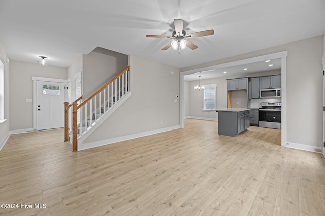 unfurnished living room with ceiling fan with notable chandelier, a wealth of natural light, and light hardwood / wood-style flooring