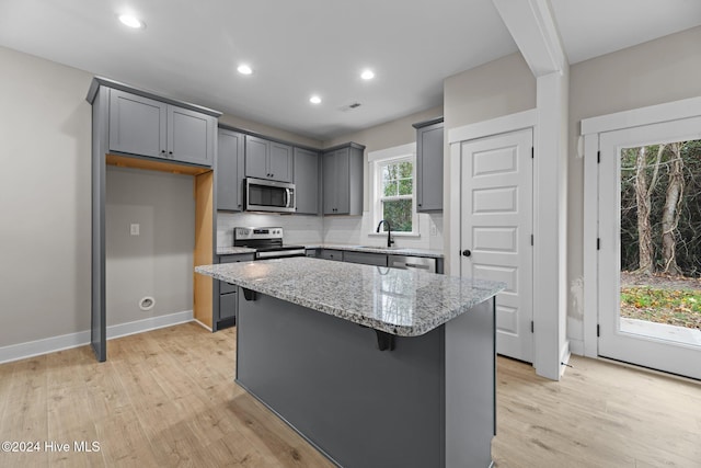 kitchen with a center island, a healthy amount of sunlight, light stone countertops, and stainless steel appliances