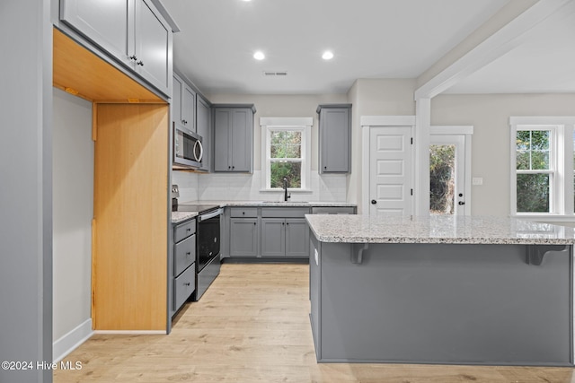 kitchen with a healthy amount of sunlight, stainless steel appliances, light stone counters, and light wood-type flooring