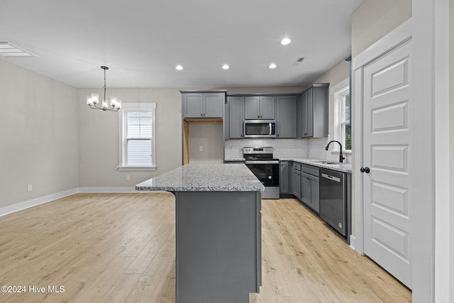 kitchen with an inviting chandelier, light stone counters, light hardwood / wood-style flooring, a kitchen island, and appliances with stainless steel finishes