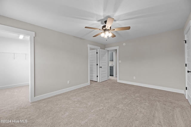 unfurnished bedroom with light carpet, a walk in closet, a closet, and ceiling fan