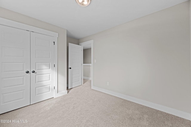 unfurnished bedroom with light colored carpet and a closet