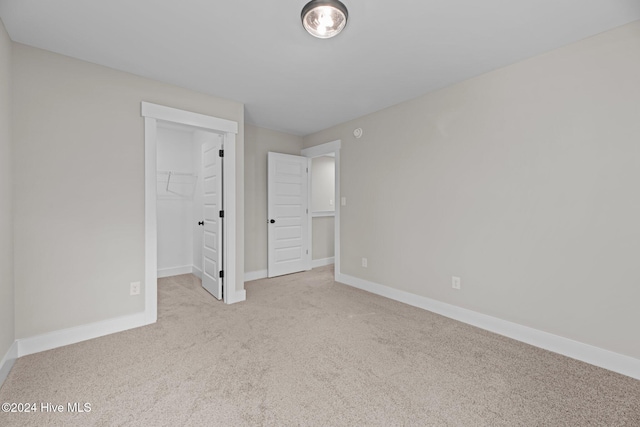 unfurnished bedroom featuring a spacious closet, light carpet, and a closet