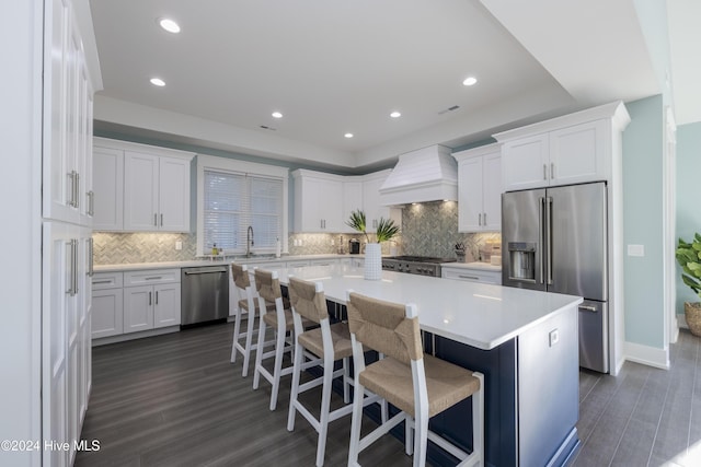 kitchen featuring a center island, custom range hood, appliances with stainless steel finishes, white cabinets, and a kitchen breakfast bar