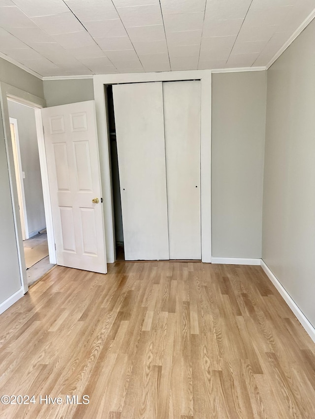 unfurnished bedroom with a closet, ornamental molding, and light hardwood / wood-style flooring