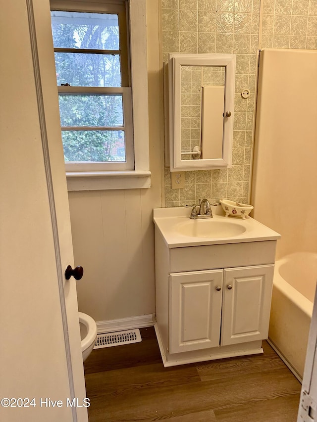 bathroom featuring hardwood / wood-style flooring, vanity, toilet, and a tub