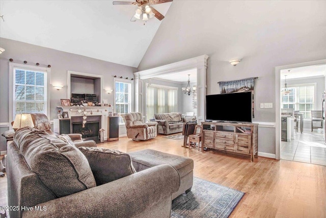 living room with a wealth of natural light, high vaulted ceiling, ceiling fan with notable chandelier, and hardwood / wood-style flooring