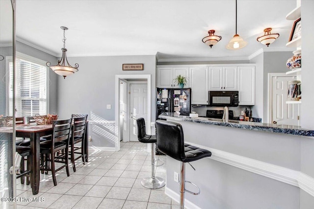 kitchen featuring dark stone counters, ornamental molding, black appliances, light tile patterned floors, and white cabinetry