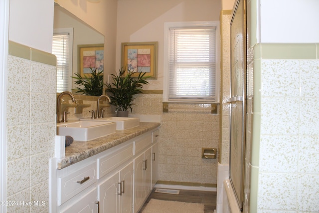 bathroom with bath / shower combo with glass door, vanity, wood-type flooring, and tile walls