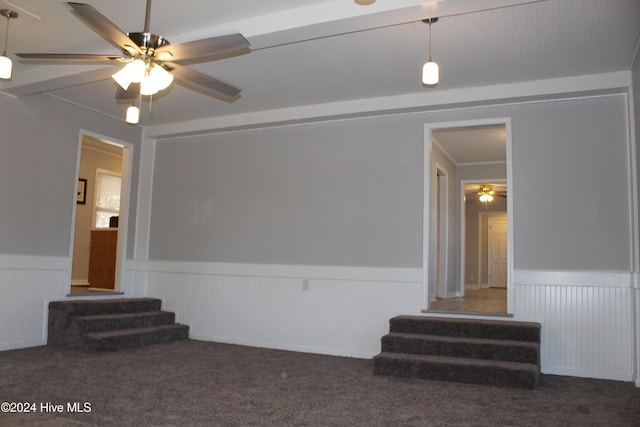 unfurnished living room featuring ceiling fan, dark carpet, and ornamental molding