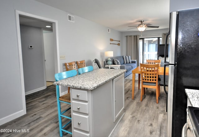 kitchen featuring a breakfast bar, light hardwood / wood-style flooring, ceiling fan, stainless steel fridge, and white cabinetry