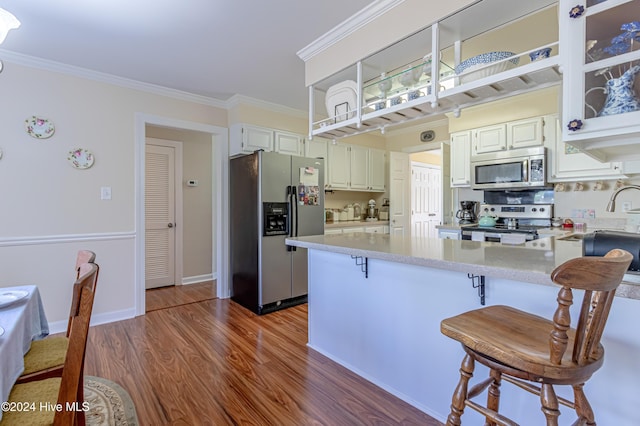 kitchen featuring stainless steel appliances, kitchen peninsula, a breakfast bar area, white cabinets, and ornamental molding