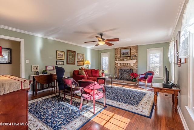 living room featuring hardwood / wood-style floors, ceiling fan, crown molding, and a brick fireplace