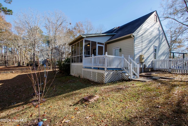 view of home's exterior with a sunroom, a wooden deck, and a lawn