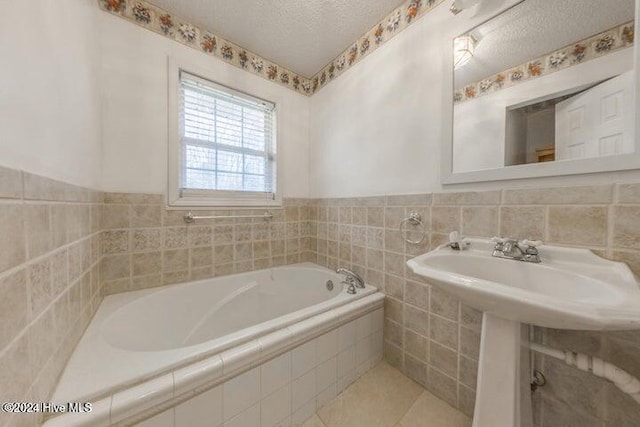 bathroom with sink, tiled tub, and a textured ceiling