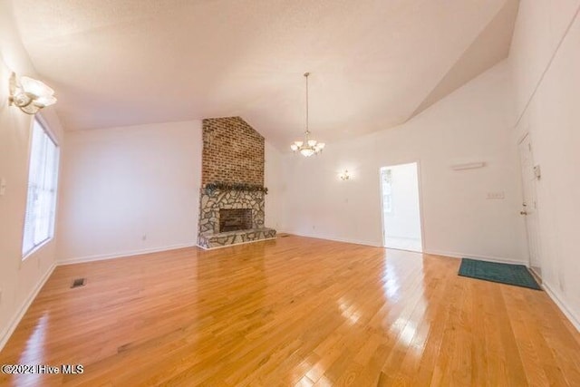 unfurnished living room with lofted ceiling, a fireplace, a notable chandelier, and hardwood / wood-style flooring