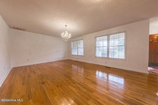 empty room featuring a textured ceiling, an inviting chandelier, and wood-type flooring