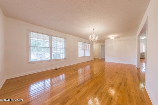 spare room with a textured ceiling, light hardwood / wood-style flooring, and an inviting chandelier